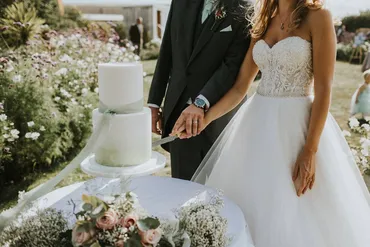 Bride and groom cutting a two-tier white wedding cake with blush roses and gypsophila in a garden